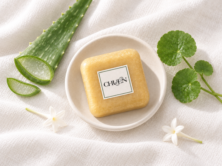 สบู่ CHUEN Gentle Care Soap บนจานสีขาว พร้อมว่านหางจระเข้ ใบบัวบก และดอกปี๊ปบนผ้าขาว